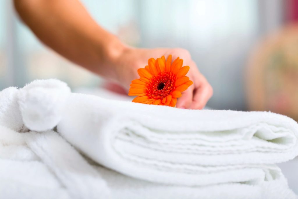 A person holding an orange flower on top of towels.