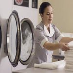 A woman in front of a dryer with some folded towels.