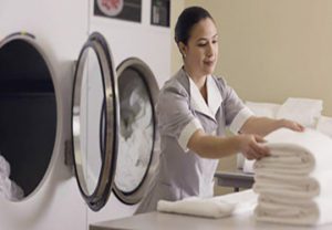 A woman in front of a dryer with some folded towels.